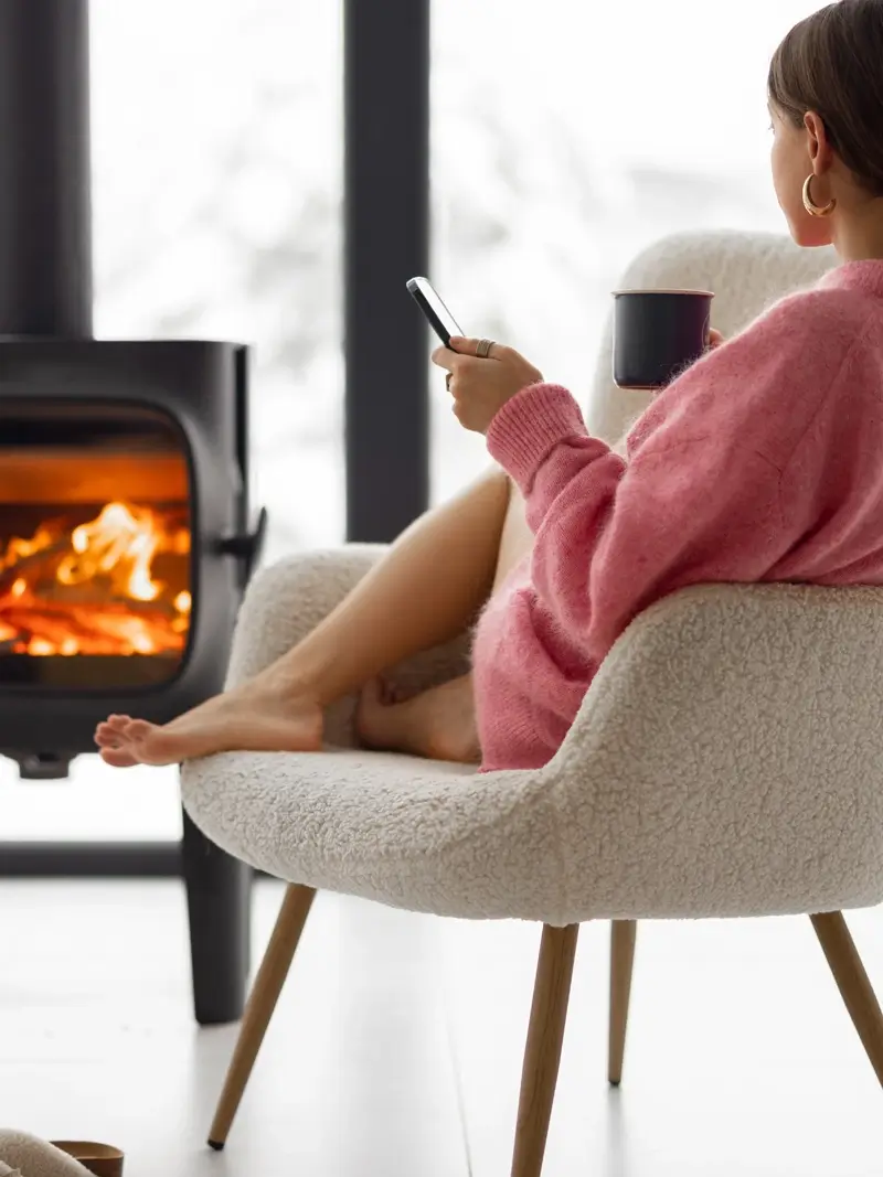 Woman with cup on chair by the fireplace at house on nature